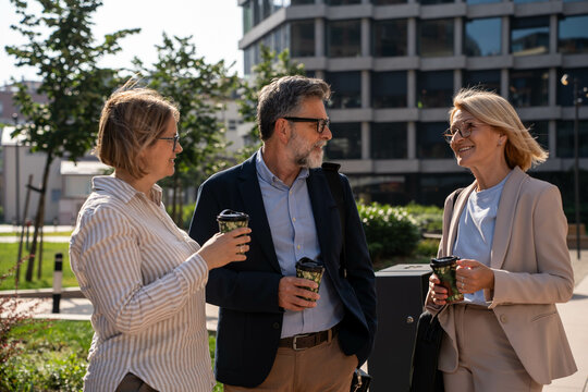 Diverse business people having coffee and water break outdoors, pleasant conversation in urban business district


