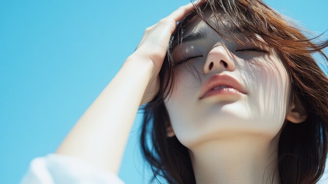 A contemplative woman touches her hair gently while facing the blue sky, radiating a sense of peace, introspection, and connection to nature in a tranquil, sunlit moment.