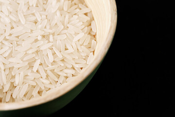 White rice grains in ceramic bowl on black background. Raw uncooked food in minimal style. Healthy carbohydrate source. Ingredient for cooking, diet, vegan or Asian cuisine.
