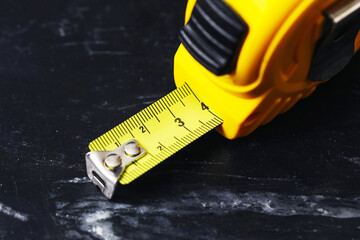Close-up of yellow measuring tape on dark blackboard surface. Precision tool for construction, DIY or tailoring. Bright color contrast for measurement concept. Simple composition.
