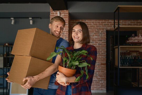 A couple enjoying moving into a new home, carrying boxes and a plant.