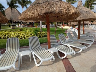 Under palapa-style umbrellas, loungers face a garden near a pool in a Riviera Maya all-inclusive resort, offering shade and tropical tranquility.