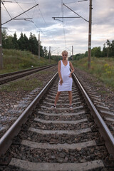 Portrait of a young beautiful blonde girl in a white blouse and summer hat on railway tracks.