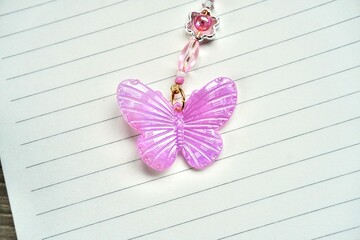 Pink buttefly beads decoration isolated on horizontal note book lined paper background.