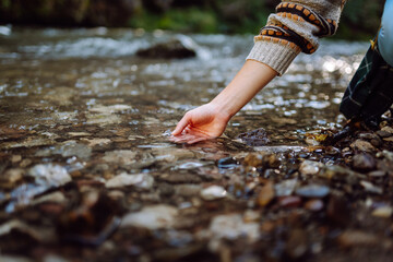Beautiful woman in hiker with bright yellow backpack on travel touching mountain river with hands and enjoying journey. Young female traveler on hiking trail in mountains. Active lifestyle. © maxbelchenko
