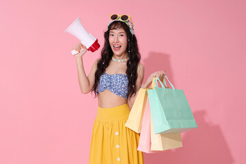 Excited Asian woman in summer outfit holding megaphone and shopping bags. Perfect for sales announcements, promotions, or summer offers.