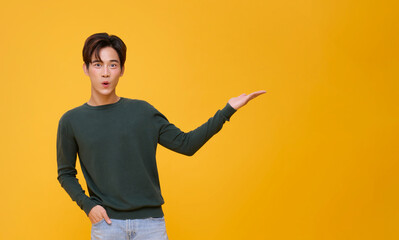 handsome asian man wow open mouth pointing finger to present something his hand gesture are perfect for the suggestion isolated on yellow copy space background.