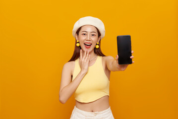 Happy beautiful young Asian woman showing smartphone mockup blank screen isolated on yellow background.