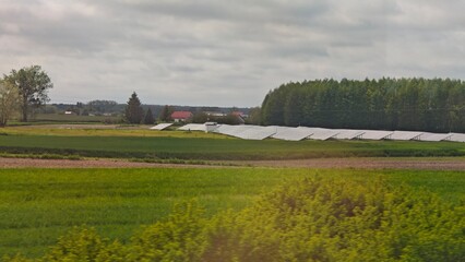 Wide rural landscape with solar panels installed on a green field near a forest and village houses....