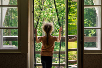 Magnetic mosquito net mesh on balcony door. Child going outdoors to home balcony through, preventing insects coming inside.