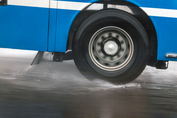 Detail of the wheel of a bus driving on a wet road during rain.