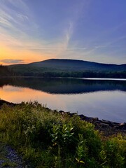 Breathtaking mountain peak at sunset. Stunning scenic view. North South Lake Campground in the Catskill Mountains. Serene summer, dusk. Clear calm blue orange purple sky clouds reflect over lake.