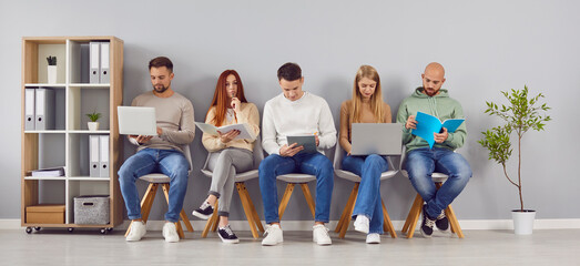 Group of young smart people office lobby chair row sitting, working with laptops, documents. Worker...