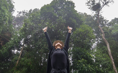 Rear view of a lady with hands up in the air in the forest