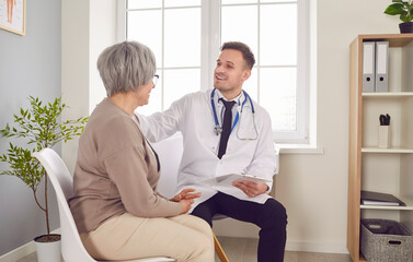 Obraz premium Senior patient in medical clinic talking with male young friendly physician wearing stethoscope and holding report file with appointment during medical examination. Doctor support concept.