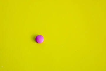 A bright pink pill is centrally placed on a vibrant yellow background. This minimalist image...