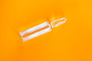 A single transparent medical ampoule is positioned on a vibrant orange background. This concise...