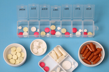Daily pill organizer box and several types of medicine on blue background