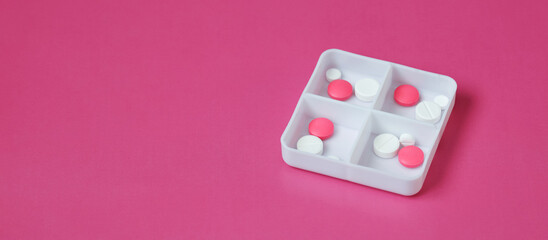 White daily pill organizer containing pink and white pills on pink background. medical backdrop with an empty space for your text