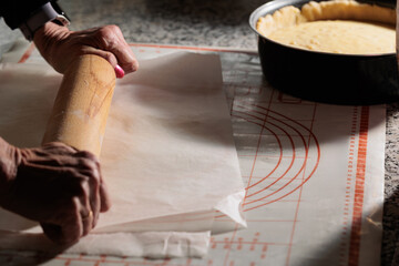 Fototapeta na wymiar mani di donna adulta che stendono parte di un impasto per una crostata dolce fatta in casa sotto un foglio di carta da forno, su un tavolo di marmo