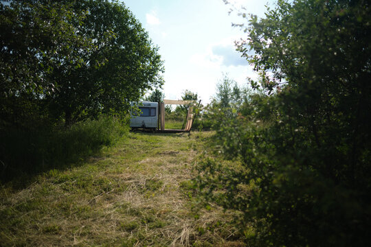 A camper van with a wooden terrace and fabric canopy is parked in the middle of tall grass and trees. This peaceful scene evokes a sense of freedom, glamping, and off-grid living.