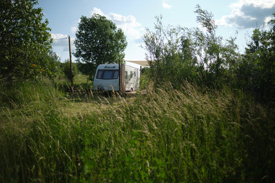 A camper van with a wooden terrace and fabric canopy is parked in the middle of tall grass and trees. This peaceful scene evokes a sense of freedom, glamping, and off-grid living.