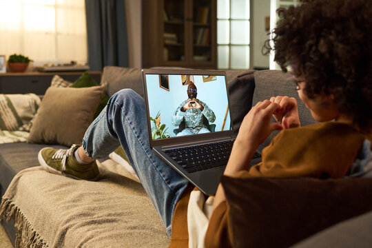 Young adult Black man in military uniform sitting on video call making heart gesture with hands, young adult Black woman sitting on sofa mirroring gesture while looking at laptop screen