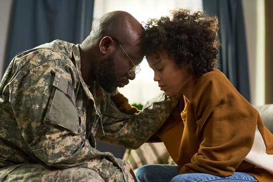 Black middle aged man in military uniform comforting Black young adult woman at home, both sitting close with foreheads touching, showing emotional family support and connection - Powered by Adobe