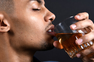 model young slim man in denim shirt sitting in armchair drinking glass of whiskey in dramatic...