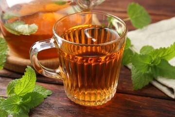 Aromatic lemon balm tea in glass cup, teapot and fresh leaves on wooden table, closeup