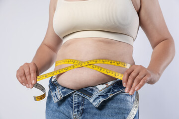 Overweight woman measuring her belly with tape on light background, closeup