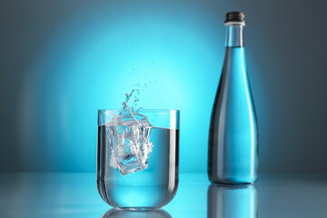 Fresh water splashing out of glass on mirror table against light blue gradient background. Backlit