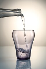 Pouring water from bottle into glass on mirror table against gray gradient background