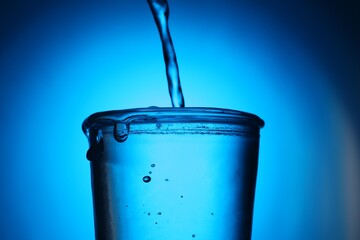 Pouring water into glass on blue gradient background, closeup. Backlit