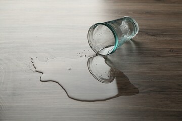 Overturned glass and spilled water on wooden table