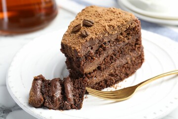 Piece of delicious chocolate cake with coffee beans and fork on white marble table, closeup