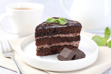 Piece of delicious cake, mint, chocolate and fork on light table, closeup
