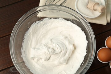 Bowl with whipped cream, whisk and ingredients on wooden table, flat lay
