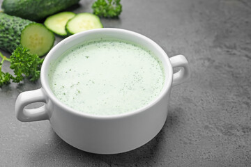Tasty cucumber soup and fresh vegetables on grey table, closeup
