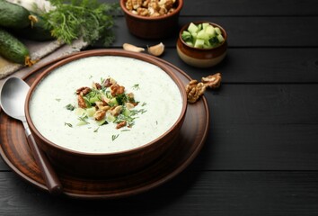 Tasty cucumber soup with dill and walnuts served on black wooden table, closeup