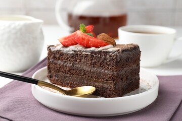 Piece of delicious chocolate cake with strawberry, almonds and tea on table, closeup