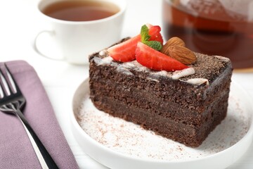 Piece of delicious chocolate cake with strawberry, almonds and tea on white table, closeup