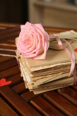 Stack of love letters, rose flower and paper heart on wooden table indoors, closeup