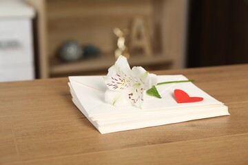 Stack of love letters, red heart and flower on wooden table indoors, closeup