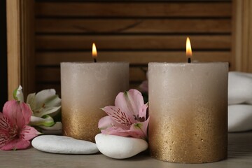 Burning candles, stones and lily flowers on wooden table, closeup