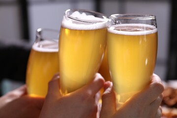 Friends clinking glasses of beer indoors, closeup