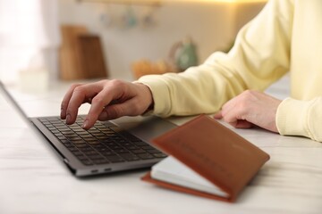 Woman using laptop at white marble table with passport indoors, closeup