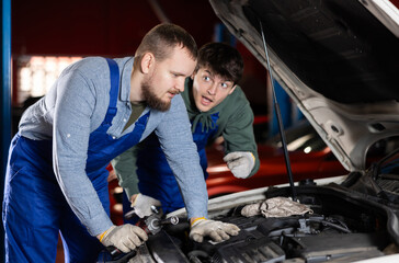 Two auto mechanics work together to diagnose an engine under the hood of a car in a repair shop