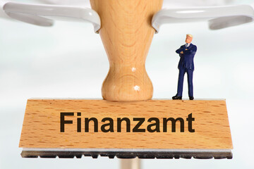 Ein Holzstempel ist beschriftet mit dem Aufdruck Finanzamt und einer Modellfigur