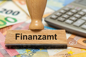Ein Holzstempel ist beschriftet mit dem Aufdruck Finanzamt auf vielen Euro Banknoten